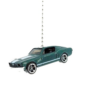 May include: A green die-cast model car with white racing stripes. The classic car has black wheels with silver rims. The car is suspended by a string of small, decorative silver ornaments, suggesting it is an ornament.