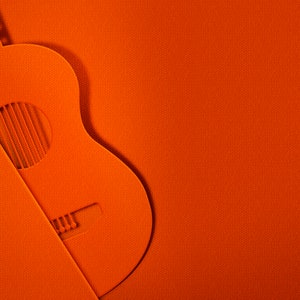 Peut inclure: Une guitare acoustique orange découpée dans du papier, sur un fond orange vif.