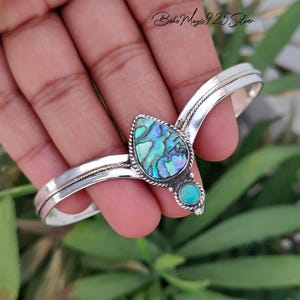 May include: A sterling silver cuff bracelet featuring a teardrop-shaped abalone shell inlay and a small round turquoise stone. The metal band has a twisted rope texture detail along the centre. The text Boho Magic 925 Silver is visible.