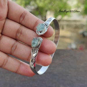 Puede incluir: Pulsera de brazalete de plata con dos acentos de piedras preciosas verde claro. La pulsera tiene un dise&ntilde;o delicado y adornado.