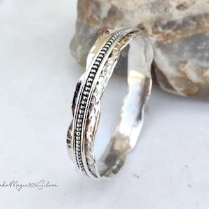 May include: A silver-colored bangle bracelet with a twisted design. The bracelet features a textured pattern and a beaded border. The words "BohoMagic925Silver" are written in cursive on the bottom left.