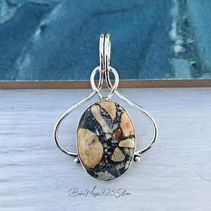 May include: A silver pendant with a knotted bail and a large oval-shaped stone. The stone is a mix of black, white, and brown colours. The text "boho magic 925 silver" is visible at the bottom of the image.