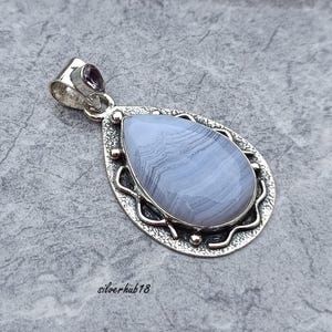 May include: A silver pendant featuring a teardrop-shaped blue agate gemstone. The pendant has an intricate silver border and a small amethyst gemstone at the top.