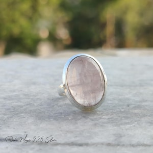 May include: A silver ring with a large oval-shaped pink gemstone. The ring is set in a simple silver band.