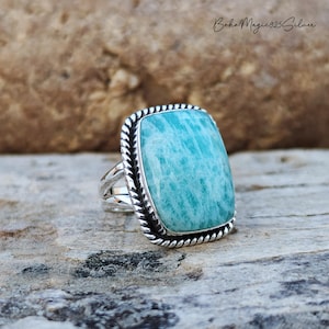 May include: A silver ring with a large, rectangular, green and blue gemstone. The ring has a rope-like design around the edge of the setting.
