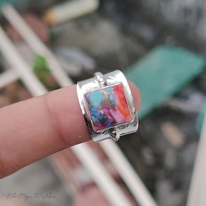 May include: A silver ring with a rectangular, multi-colored stone. The stone features shades of turquoise, purple, and orange. The ring is marked with the text "Boho Magic 925 Silver".