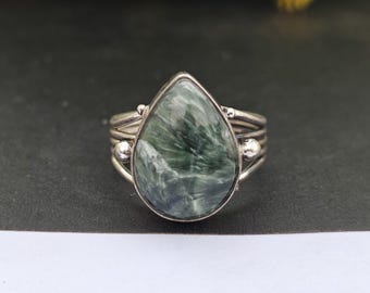 May include: A silver ring featuring a teardrop-shaped green and white gemstone. The ring has a delicate band with three silver bands and two small silver beads.