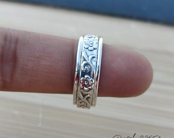 May include: A silver ring with a floral design. The ring is worn on a finger.