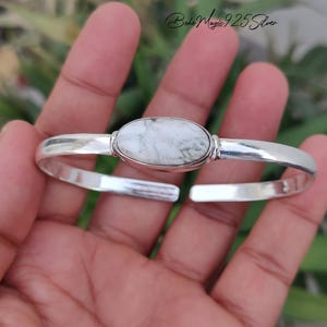 May include: A polished 925 sterling silver cuff bracelet featuring a central oval-shaped white stone with grey veining. The metal band is smooth and reflective, with an open design. The text Boho Magic 925 Silver is visible in the upper corner.