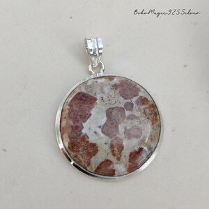 May include: A round pendant featuring a brown and white stone set in sterling silver. The stone has a distinctive pattern of brown and white swirls.