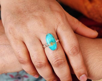 May include: A silver ring with a turquoise oval gemstone. The turquoise is a vibrant blue-green color with brown veins.