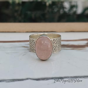 May include: A silver ring with a delicate floral design and a pale pink oval gemstone.