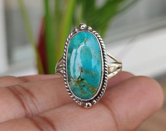 May include: Oval turquoise ring with a silver band. The turquoise stone is a vibrant blue-green color with brown veining. The ring has a detailed, braided border and split shank design.