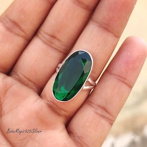 May include: A silver ring featuring a large, oval-cut, emerald-green gemstone. The ring's band is split at the top, creating a unique design. The text "Boho Magic 925 Silver" is visible at the bottom left.
