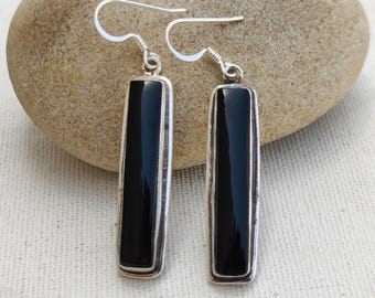 May include: A pair of silver earrings with rectangular black onyx stones. The earrings have a simple, elegant design with a polished finish. The earrings are displayed on a neutral background.