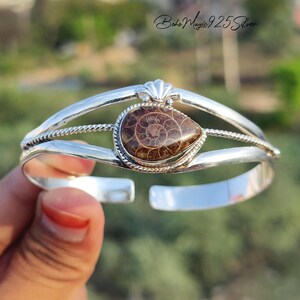 May include: A silver cuff bracelet featuring a teardrop-shaped, fossilized ammonite stone. The bracelet has a detailed design with a shell-shaped accent and the text "Boho Magic 925 Silver".
