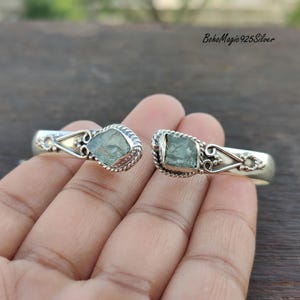 Puede incluir: Pulsera de brazalete de plata con dos piedras preciosas de aguamarina. La pulsera tiene un dise&ntilde;o delicado y adornado con un patr&oacute;n de cuerda trenzada.