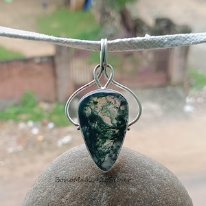 May include: A silver pendant with a green and white moss agate stone. The pendant is in the shape of a teardrop and has a delicate silver bail.