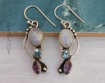 May include: A pair of sterling silver drop earrings featuring a vertical arrangement of three gemstones: a round iridescent moonstone at the top, a small round blue topaz in the center, and a marquise-cut purple amethyst at the bottom.