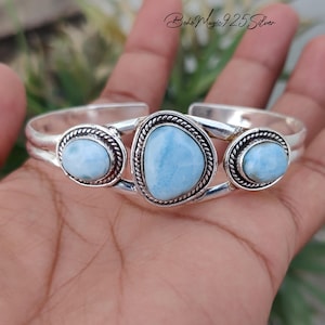 May include: A silver cuff bracelet featuring three light blue, oval-shaped Larimar stones set in twisted metal frames. The central stone is larger than the two flanking stones. The text "Boho Magic 925 Silver" is visible in the upper right corner.