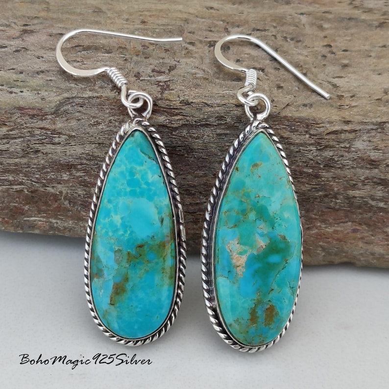May include: A pair of turquoise teardrop earrings with a silver rope-like border. The turquoise stones have a mottled blue-green color. The earrings have a simple hook closure. The text "BohoMagic925Silver" is at the bottom.