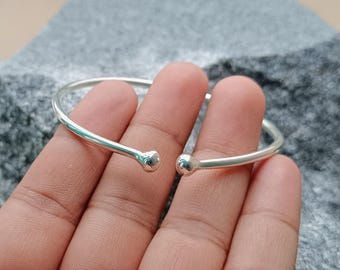 Op de afbeelding: Een eenvoudige zilveren armband met afgeronde uiteinden. De armband is open en heeft een gladde, gepolijste afwerking.