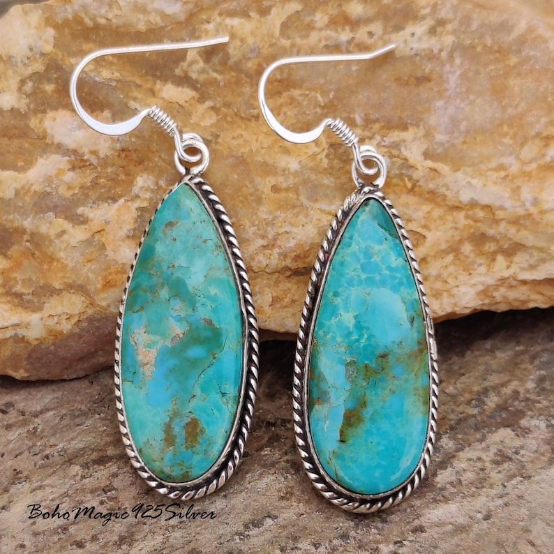 May include: A pair of turquoise teardrop earrings with a silver rope-like border and hook. The earrings have a bright blue-green color with brown marbling. The text "Boho Magic 925 Silver" is visible at the bottom.