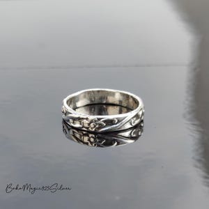 Puede incluir: Un anillo de banda de plata con un diseño floral. El anillo es simple y elegante.