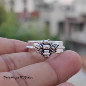 May include: A silver spinning ring with a bee design. The ring is on a finger.