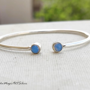 May include: A silver-coloured open cuff bracelet with a light blue stone at each end. The bracelet has a simple, elegant design with a smooth, polished finish. The text "BohoMagic 925Silver" is at the bottom.