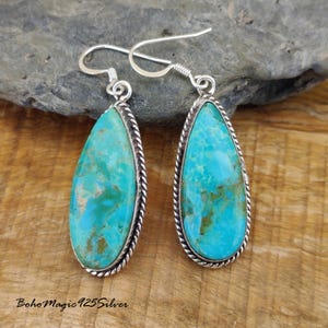 May include: A pair of turquoise teardrop earrings with a silver rope-like border. The turquoise stones have a marbled appearance with shades of blue and green. The earrings have a simple hook closure.