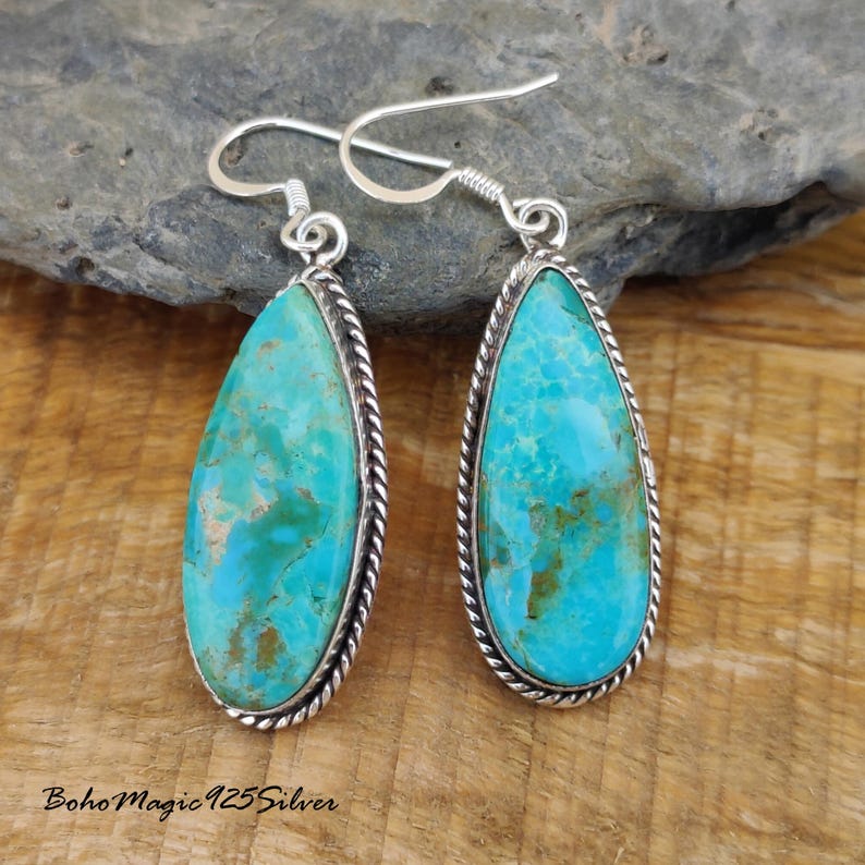 May include: A pair of turquoise teardrop earrings with a silver rope-like border. The turquoise stones have a marbled appearance with shades of blue and green. The earrings have a simple hook closure.