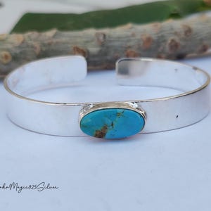 May include: A silver cuff bracelet featuring a turquoise stone. The bracelet has a polished finish and an open design. The turquoise stone is oval and set in a silver bezel. The bracelet is likely made of sterling silver.
