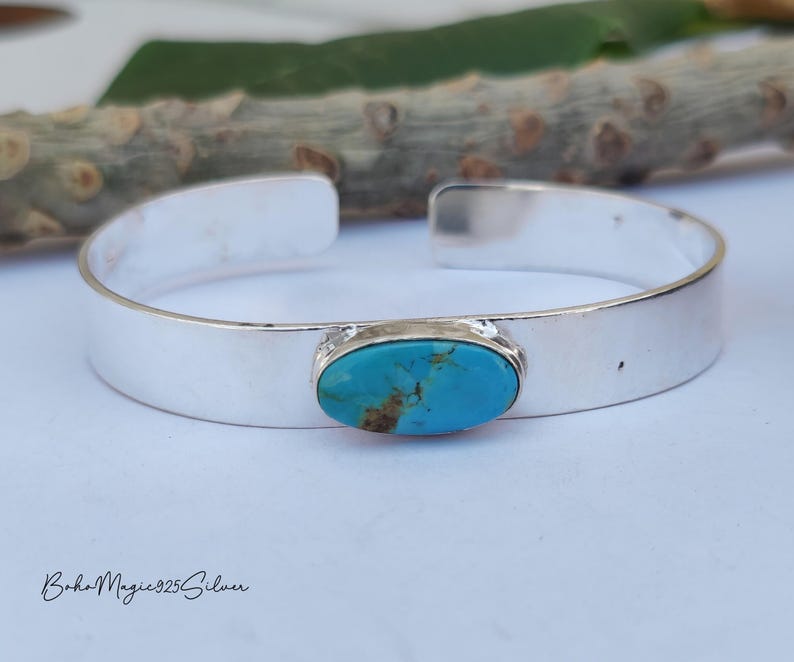 May include: A silver cuff bracelet featuring a turquoise stone. The bracelet has a polished finish and an open design. The turquoise stone is oval and set in a silver bezel. The bracelet is likely made of sterling silver.