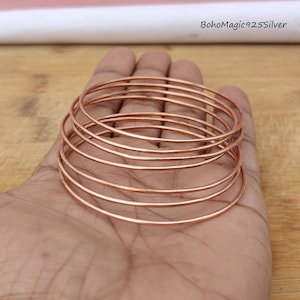 May include: A set of seven rose gold bangles, stacked on top of each other. The bangles are thin and have a smooth, polished finish.