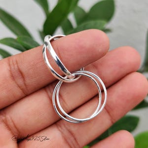 May include: A set of three interlocking silver rings with a smooth, polished finish. The rings are connected to form a single unit, featuring a bright, reflective metallic surface that catches the light. The design consists of three thin, circular bands.