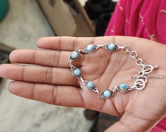 May include: A silver bracelet with a light blue gemstone accents. The bracelet has a toggle clasp.