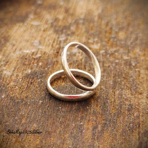 May include: Two silver rings, one resting atop the other, against a rustic wooden background. The rings are smooth and shiny, reflecting light. The rings are likely wedding bands or promise rings.