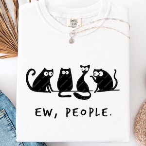 Puede incluir: Camiseta blanca con un gráfico negro de cuatro gatos y el texto "EW, PEOPLE." Los gatos están en varias poses, uno de ellos saludando. La camiseta está hecha de un material suave y tiene cuello redondo.