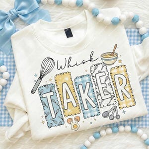 May include: Cream-coloured sweatshirt featuring the words "Whisk Taker". The design includes a whisk, mixing bowl, and the letters of "TAKER" in blue and yellow plaid patterns. A fun, baking-themed graphic.