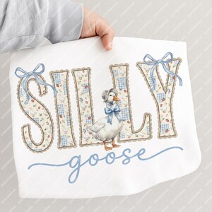 May include: White baby blanket featuring the words "SILLY goose" in blue script. The letters are decorated with a floral and gingham pattern, and a watercolor illustration of a goose wearing a bonnet and bow.