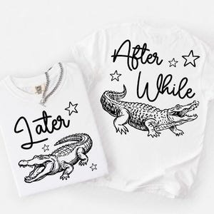 May include: Two white t-shirts featuring black line art illustrations of crocodiles. One shirt displays the word Later with a crocodile and stars, while the other shirt displays the words After While with a crocodile and stars in a matching style.