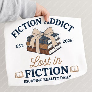 May include: White tote bag with the text "FICTION ADDICT" and "Lost in FICTION" in navy blue and brown. The design includes a stack of books tied with a beige bow and the words "Escaping Reality Daily".