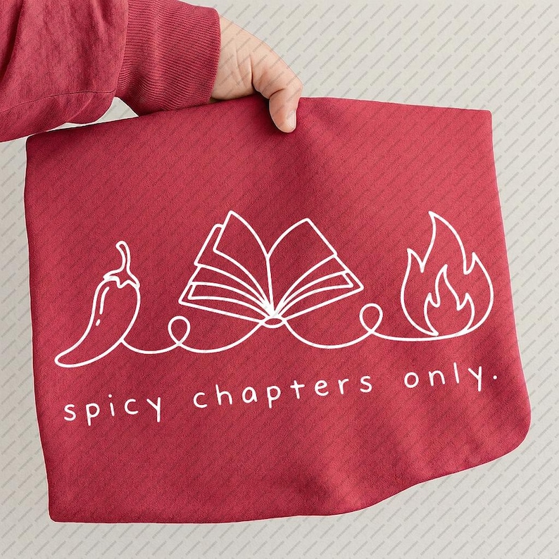May include: A red fabric item with a white graphic of a chili pepper, an open book, and flames, connected by a line. The text "spicy chapters only" is below the graphic. The item is held by a person.
