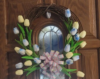 May include: A spring wreath with a pink and white bow, decorated with blue and yellow tulips.
