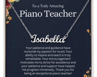 May include: A silver necklace with the name "Isabella" on it, in a white box with a blue background and a floral design. The box also includes a message thanking a piano teacher for their guidance and support.