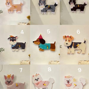 Pode incluir: Nove relógios de parede com formato de cão de diferentes raças e cores. Cada relógio tem um chapéu de festa ou uma coroa na cabeça e um mostrador com ponteiros.