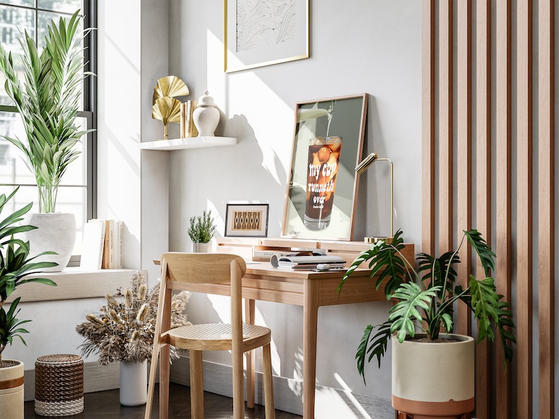 Pu&ograve; includere: Un ambiente di lavoro domestico con una scrivania in legno, una sedia e una stampa incorniciata con il testo "my cup runneth over". La scrivania ha una lampada, una pianta in vaso e un laptop. La stanza ha una grande finestra, una pianta in vaso e uno scaffale con oggetti decorativi.