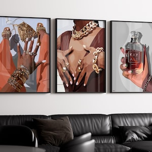 May include: Set of three framed art prints. The prints depict illustrations of hands adorned with gold jewelry, and a perfume bottle. The first print shows hands with rings and bracelets. The second print shows a person wearing a gold necklace and bracelets. The third print shows a perfume bottle with the text "KAY ALI".