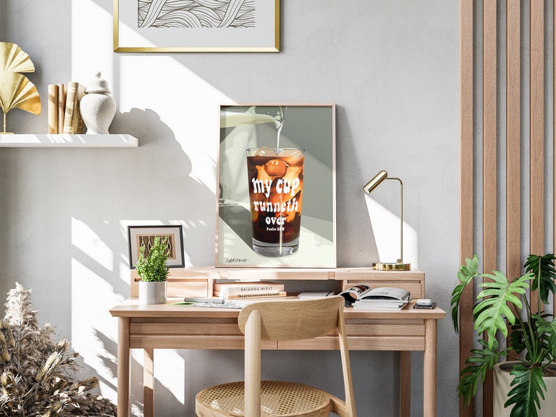 Pu&ograve; includere: Una stampa incorniciata di un bicchiere di caff&egrave; freddo con il testo "my cup runneth over" in lettere bianche. La stampa &egrave; su uno sfondo verde chiaro e si trova su una scrivania di legno.